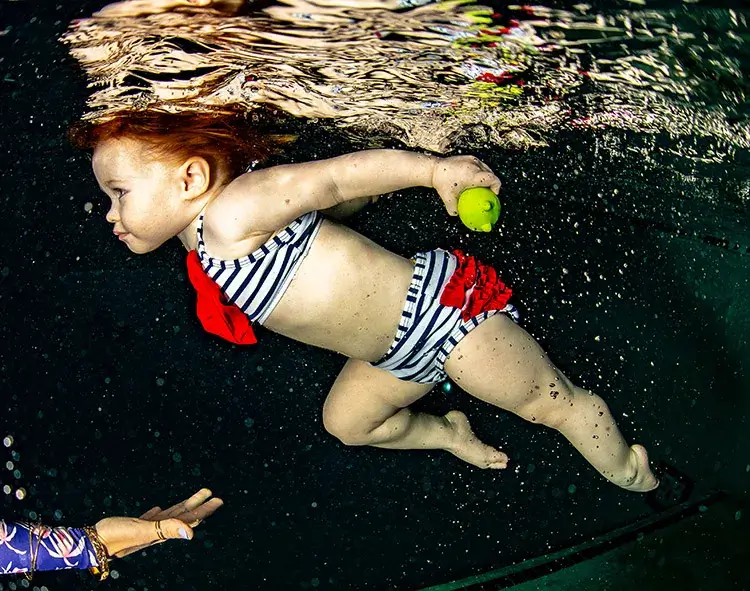 An infant confidently swimming underwater with hands reaching out.