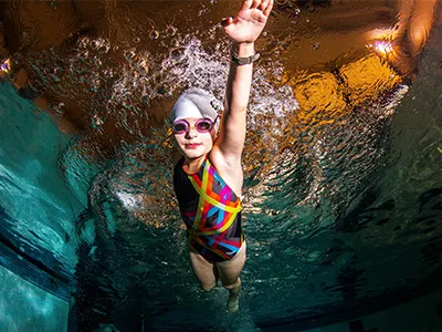 A young girl in a swimsuit with a swim cap practices her stroke technique beneath the surface of the pool as she trains for competitive swimming.
