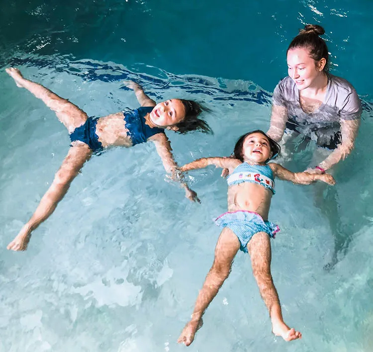 A young female Flipkick swim instructor helping two young children float on their backs in a swimming pool.