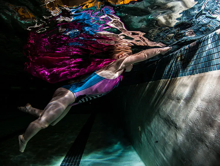 A swimmer in a colorful swimsuit glides underwater in a pool, arms extended forward, practicing her stroke.