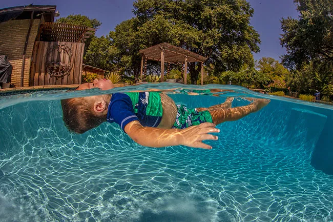 A young boy in swimwear floats on his back in an outdoor pool.